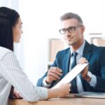 insurance agent pointing at clipboard in clients hand at tabletop in office, house insurance concept