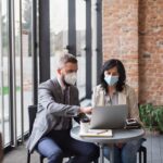 Portrait of businesspeople sitting at the table and working indoors, coronavirus concept.